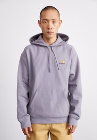 Purple hoodie made of soft fabric with a front pocket. Features adjustable drawstring hood and a small logo in yellow and red.