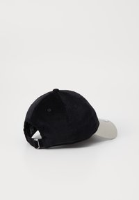 Sort kordfløjl baseballcap med en cremefarvet skygge og justerbar rem bagpå. Har simpel syning og ventilationshuller.