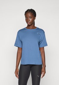 Blauwe korthals T-shirt van zacht materiaal, met een ronde hals en een klein logo op de linkerborst. Gecombineerd met zwarte leggings.