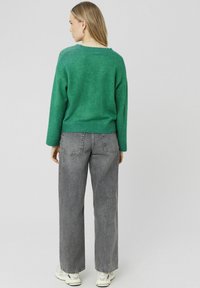 Pull en mélange de laine vert avec une coupe décontractée, col rond et ourlet côtelé, assorti à un jean en denim gris taille haute.