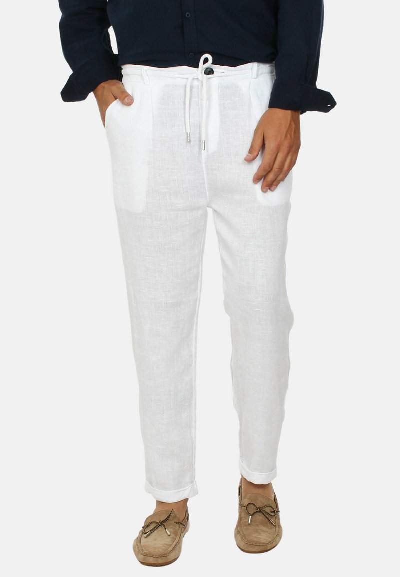 Pantaloni bianchi in lino con vita elasticizzata, due tasche laterali e polsini. Il tessuto ha una leggera texture ed è abbinato a scarpe casual.