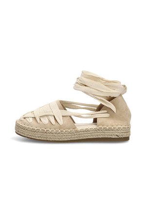 Espadrilla beige plana con suela de yute tejido, puntera cerrada y tiras de tela para atar al tobillo alrededor de la pierna.