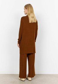 Hnedý pletený outfit obsahujúci dlhý rukáv top a široké nohavice. Tkanina má jemnú štruktúru a dizajn je uvoľnený s bočnými prieramkami.