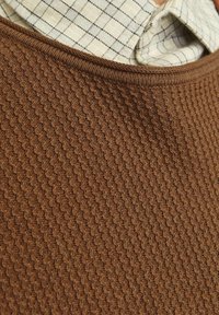 Suéter marrón texturizado con un patrón de punto, que presenta un cuello acanalado y una superposición de una camisa de cuadros clara debajo.