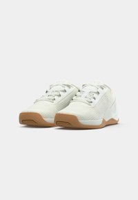 Een paar witte mesh sneakers met beige rubberen zolen, vetersluiting aan de voorkant en minimalistische branding op de tong en zijkant.