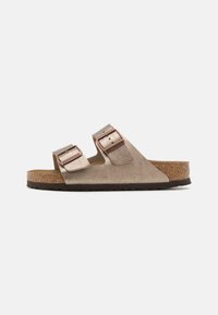 Sandale Birkenstock cu două catarame metalice ajustabile, brâu texturat de culoare bej și talpă din plută, având o talpă din cauciuc maroniu.