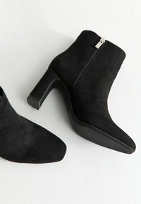 Stivaletti in suede nero con punta affusolata, chiusura con cerniera e tacco a blocco. Suola texturizzata per una migliore presa. Design moderno e slanciato.