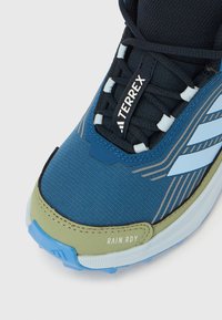 Μπλε και μαύρο παπούτσι Adidas Terrex για πεζοπορία με ανοιχτοπράσινο κάλυμμα στο μπροστινό μέρος, λευκές ρίγες, μαύρα κορδόνια και ετικέτα "RAIN.RDY" στη σόλα.