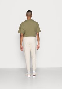 Op maat geknipt olijfgroen t-shirt met korte mouwen, gecombineerd met crèmekleurige tapered broeken en witte sneakers met rode accenten. Glad stoftextuur.
