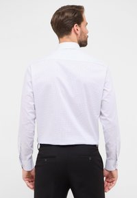 Camicia a maniche lunghe di colore bianco con un leggero motivo a quadri in viola chiaro. Presenta un colletto button-down e polsini regolabili. Vestibilità sartoriale.