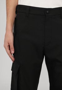Svarta cargo-byxor med platt front, bältesöglor och en ficka på sidan. Tillverkade av ett slätt tyg med en strukturerad passform.