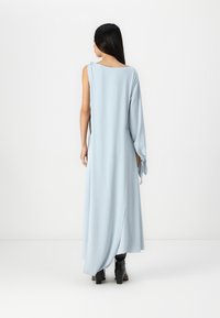 Μακριά, ανοιχτό μπλε φόρεμα από λείο ύφασμα με χαλαρή εφαρμογή. Διαθέτει σχέδιο με έναν ώμο και πλάγιο σκίσιμο, συνδυασμένο με μαύρες ψηλοτάκουνες μπότες.