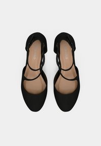Črne čevlje s ravnim dizajnom, ki imajo križne trakove in odprt prst. Material izgleda gladko, enobarven in brez vidnih vzorcev.