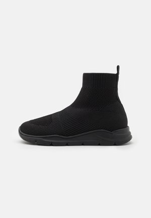 Zapatilla negra de punto hasta el tobillo con un patrón texturizado, suela flexible y cuello acolchado. Incluye una lengüeta para facilitar el calzado.