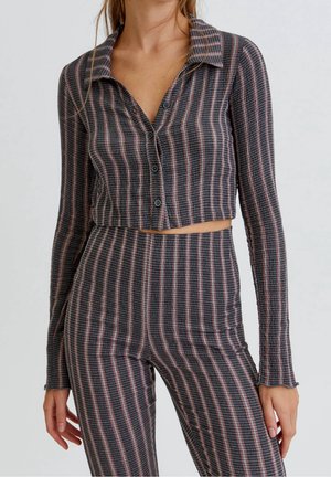 Femme portant un crop top à manches longues boutonné et un pantalon taille haute assorti avec un motif rayé vertical.