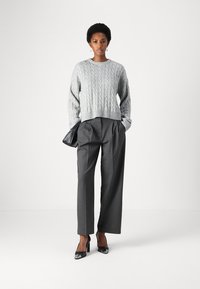 Szürke cable-knit pulóver széles szegéllyel, magas derekú, csíkos nadrággal és fényes fekete magassarkúval párosítva. Fekete kézitáska tartozék.