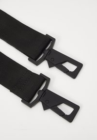 Schwarze Nylonriemen mit strukturierten Oberflächen, ausgestattet mit zwei schwarzen Kunststoffschnallen mit einem einzigartigen Verschlussdesign für sicheren Halt.