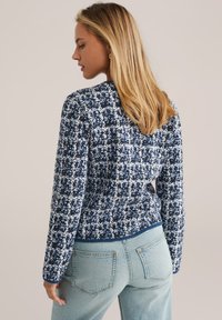 Navy and white patterned knitted sweater with a round neckline, long sleeves, and a cropped design. Features ribbed cuffs and hem.