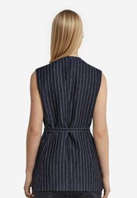 Mörkblå ärmlös topp med vita vertikala ränder, insnörad i midjan med ett matchande bälte. Har en ren design på ryggen med hög halsringning.