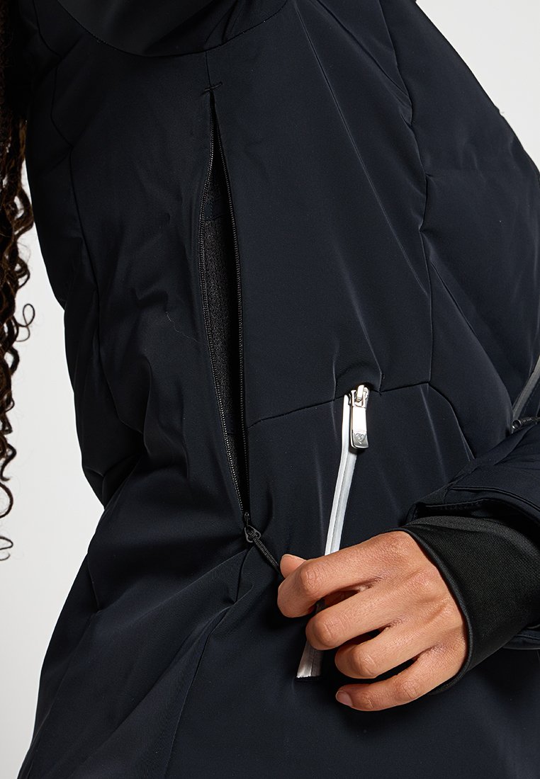 Zwarte pufferjack met een zijrits, voorzien van een glanzende zilveren trekhaak. De stof lijkt glad met een gestikt patroon.