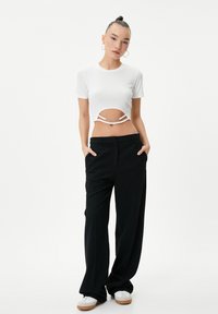 Hvid ribbet cropped top med udskæring og kæde detaljer, parret med højtaljede sorte brede bukser og hvide sneakers. Enkle hoops øreringe.