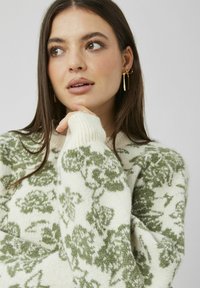 Pull en tricot crème avec motif floral vert. Comprend des poignets et un col côtelés, une texture douce et une coupe décontractée.
