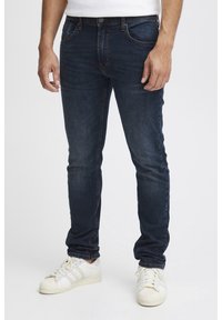 Mörkblå denimjeans med slim fit, fem fickor och subtila sömnadsdetaljer. I kombination med vita sportskor.