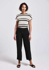 Haut en tricot avec une base crème et des rayures noires, associé à un pantalon noir ample avec une taille à cordon. Sandales plates noires.