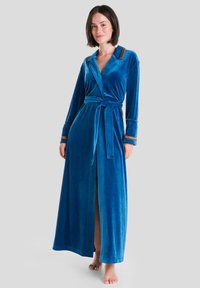 Ropa larga de terciopelo azul con diseño tipo envoltura, cintura ceñida con cinturón y acentos marrones contrastantes en el cuello y los puños. Textura suave y lisa.