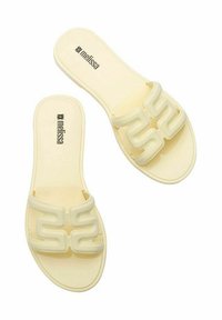 Chanclas amarillas con una correa blanca gruesa y curvada que presenta un diseño ondulado. Textura suave y suela plana, con la marca "melissa" en la plantilla.