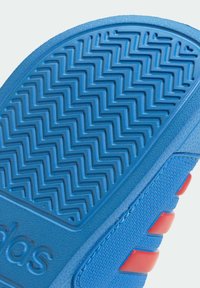 Niebieska gumowa podeszwa buta z zygzakowatym wzorem bieżnika, wykonana z fakturowanego niebieskiego materiału z czerwonymi akcentami po bokach.