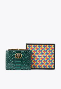 Teal groene leren portefeuille met een gouden sluiting, versierd met een slangeontwerp, naast een kleurrijk gestructureerde Kurt Geiger London doos.