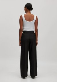 Witte aansluitende tanktop met brede bandjes, gecombineerd met zwarte hoge taille, wijde leg trousers. Gladde stof, strakke lijnen, geen zichtbare patronen.