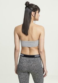 Grijze cropped tube-top en zwarte legging met tailleband met de tekst "URBASICS". De stof is soepel en rekbaar; de top heeft een aangesloten ontwerp.