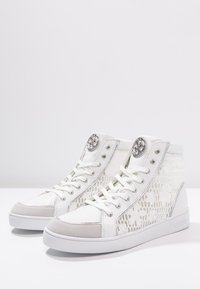 Zapatillas altas de material sintético blanco con acentos texturizados, diseño con cordones y herrajes plateados en la lengüeta y en el lateral.