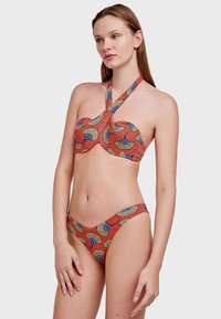 Bikini u crveno-plavom uzorku s halter krojem, s naramenicom sa čvorom i niskim donjim dijelom, izrađen od rastezljivog materijala.
