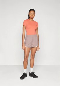 Lühikeste varrukatega korallikarva topp, millel on helepruunid lühikesed püksid valge äärisega, kantud mustade kingade ja valgete sokkidega. Sile kangas, igapäevane stiil.