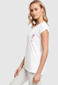 White cotton t-shirt with rolled sleeves featuring colorful drink and flower embroidery on the chest. Soft texture, loose fit, and casual style.