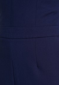 Marinblått tyg med en jämn textur och en lätt glans, med en ren söm längs midjan och utan synlig hårdvara eller mönster.