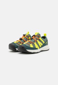 Grønn og gul nett-sneaker med oransje skolisser, teksturert overdel, gummisåle og grep for enkel påføring. Merkbare ventilasjonsstriper.