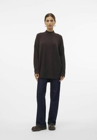 Pull oversized à col haut en tissu marron foncé, associé à un pantalon en denim foncé et des bottes marron épaisses. Design simple et décontracté.