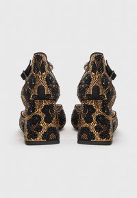 Μαύρα και χρυσά ψηλοτάκουνα παπούτσια με μοτίβο λεοπάρδαλης, διαθέτουν χοντρό τακούνι, λουράκι στον αστράγαλο και υφασμένες επιφάνειες.