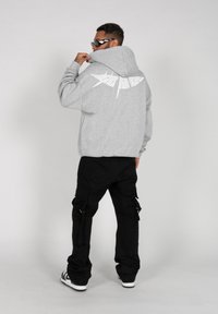 Grå hettegenser med hvit grafisk design på baksiden, sammen med svarte cargo-bukser og sporty hvite joggesko.