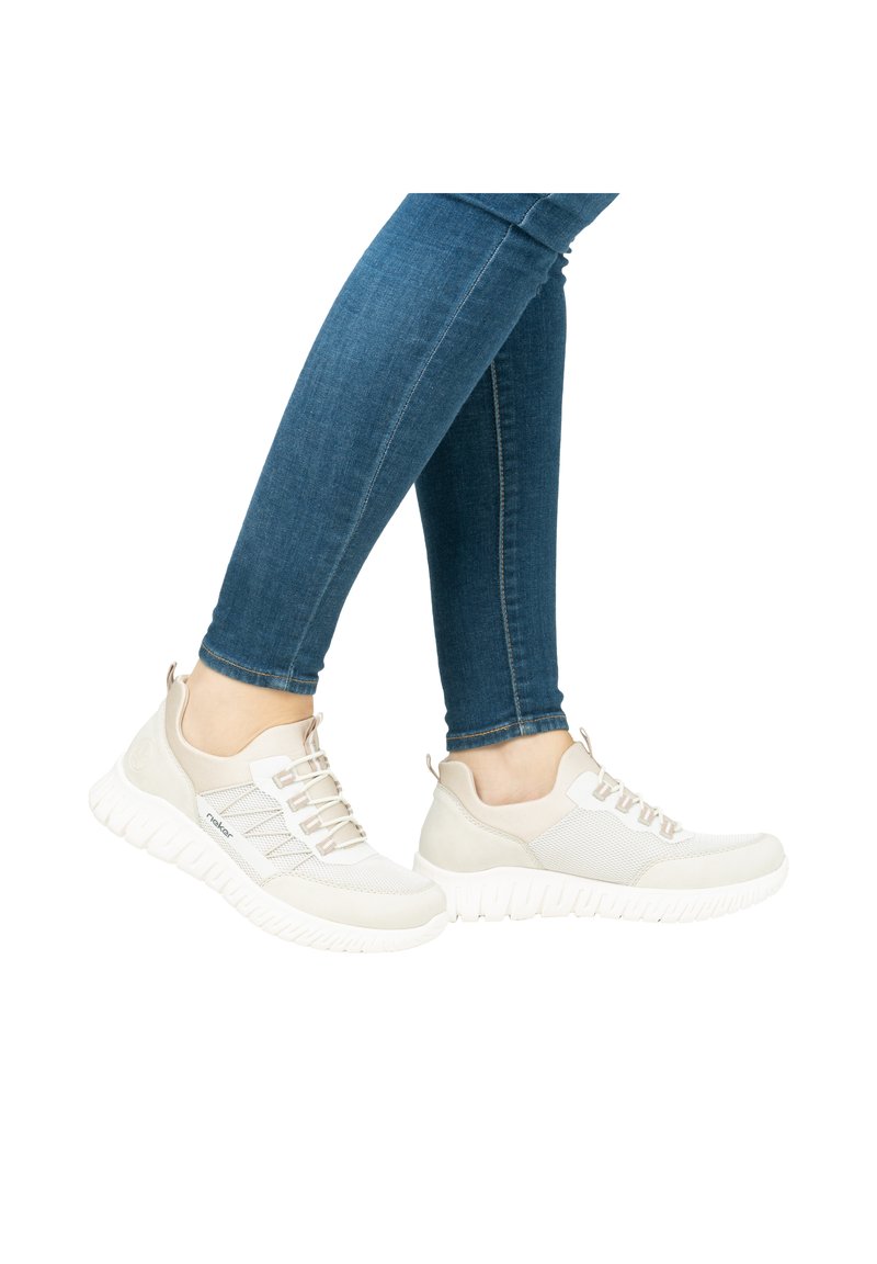 Helle graue Sneakers mit einer strukturierten Mesh-Oberfläche, elastischen Schnürsenkeln und einer klobigen weißen Sohle. Getragen mit blauen engen Jeans.