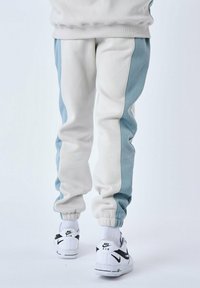 Pantalones de chándal en gris claro y azul cielo con un corte relajado, que presentan puños acanalados y detalles en los paneles laterales, combinados con zapatillas blancas de Nike.