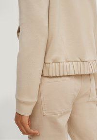 Lichtbeige sweater met ribbels aan de cuffs en zoom, gemaakt van zacht materiaal. De stof heeft een gladde textuur en een ontspannen pasvorm.