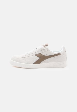 Baskets en suède blanc avec un logo latéral marron, bout rond, design à lacets et semelle en caoutchouc blanc avec des accents texturés.