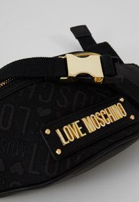 Černá látková ledvinka s embosovaným logem "LOVE MOSCHINO" a zlatými kovovými doplňky, vybavená pevnou přezkou a texturovanými detaily.