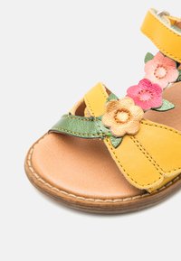 Gelbe Leder-Sandale mit floralen Akzenten in Pink, Orange und Grün. Offene Zehenpartie mit gestickten Details und einer hellbraunen Innensohle.