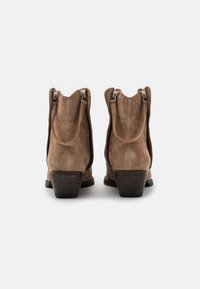 Botas de tobillo de ante marrón con un borde curvado, cremalleras laterales y un tacón de madera apilado. Textura suave con acentos mínimos.
